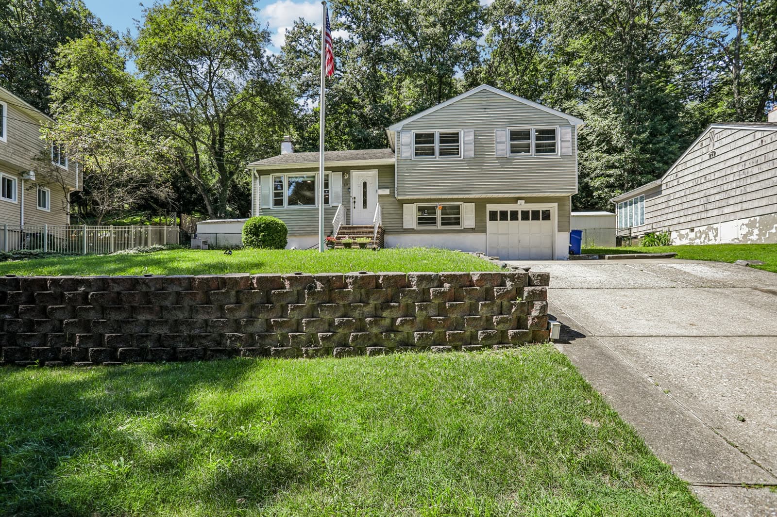 Front of the split-level home with a stone retaining wall, a sloped lawn and a flagpole
